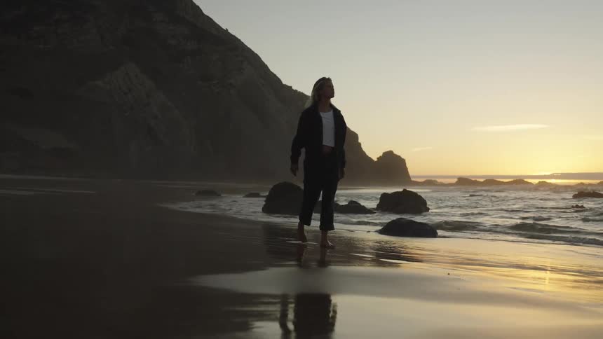 Woman walking barefoot on the wet sand during sunset by the sea