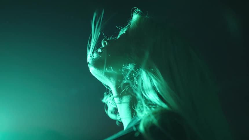 Woman lit by green light looking upward with hair blowing in the wind