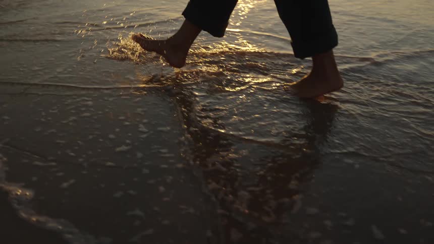 Person in rolled up jeans walking along the sandy shoreline at dusk