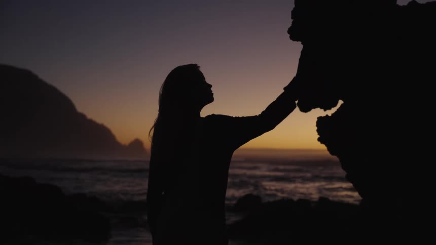 Woman touching a rock formation by the sea during sunset