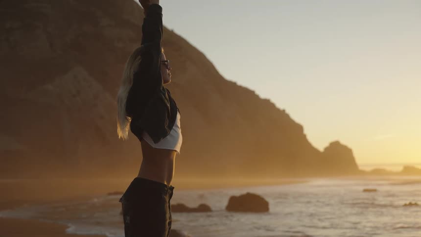 Woman with arms raised watches the sunset on the beach