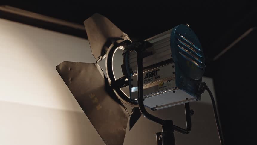 A studio arri light with barn doors sits on a stand in a dim set