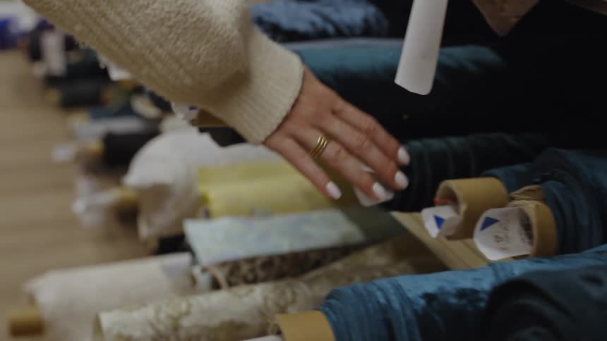 Hand touching fabric rolls displayed on shelves in a sewing store