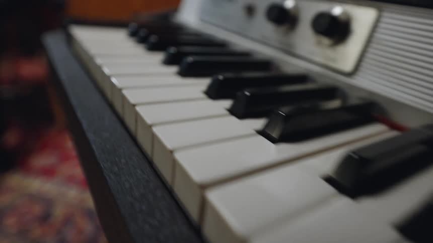 A close angled view focuses on the white and black keys of a vintage rhodes electric piano with knobs visible on the upper panel and the keys appearing slightly worn