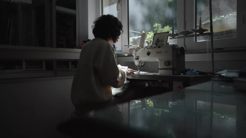 Person sewing on a machine near a window with natural light entering the room
