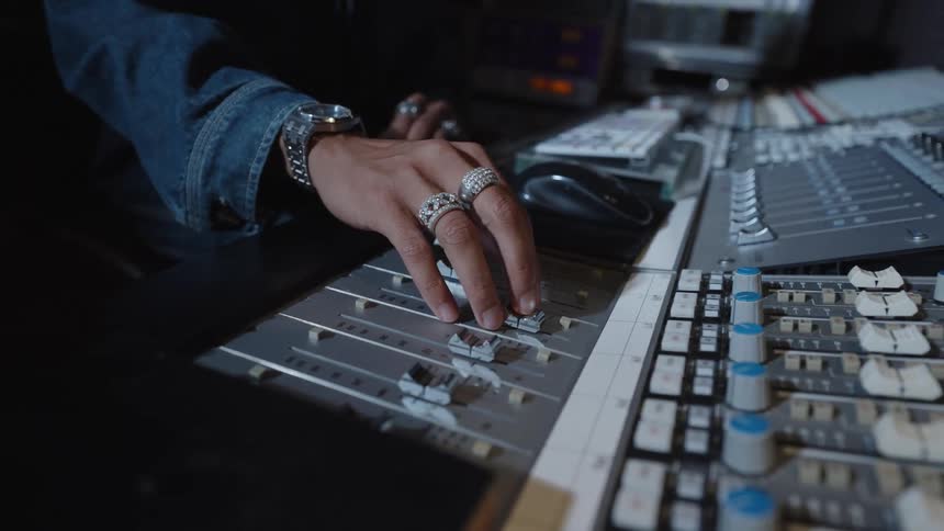 Hand adjusting controls on a mixing console in a recording studio