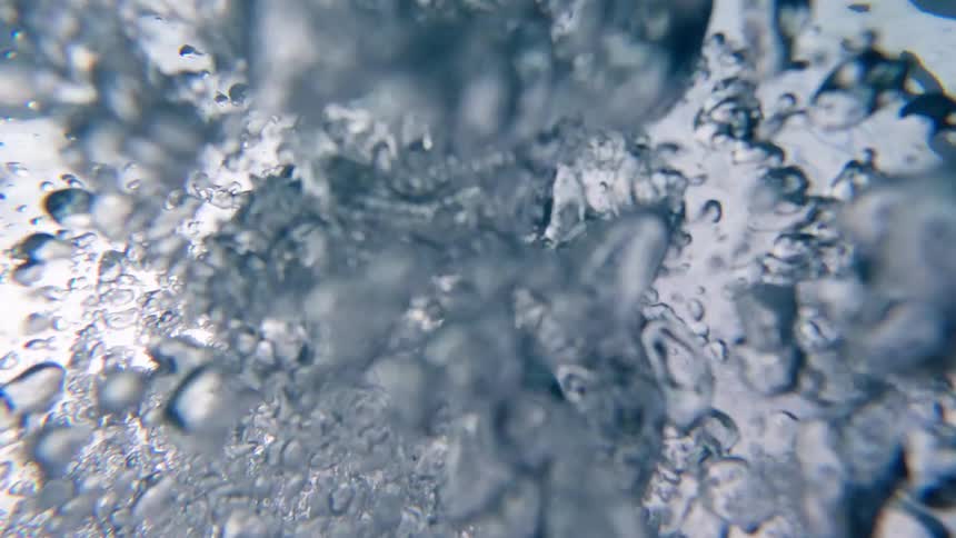 The video is an extreme closeup shot from underwater showing clear air bubbles rapidly rising through a mediumgray liquid the bubbles are of varying sizes and are highly detailed suggesting a fast movement or sudden injection of air