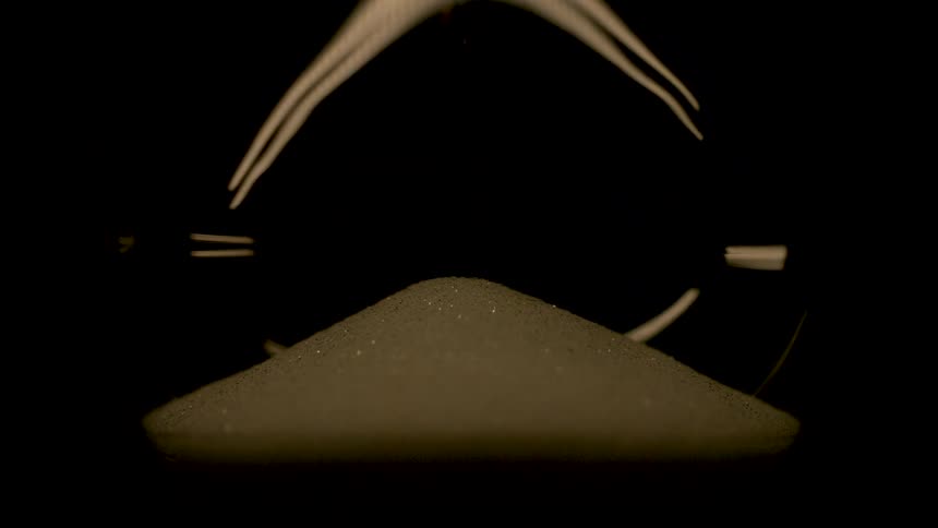 A small mound of sand dramatically lit beneath curved light streaks in a dark space