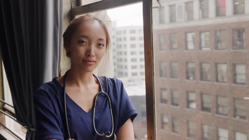 Close up portrait of a young asian female healthcare professional standing by the window in a room during daytime