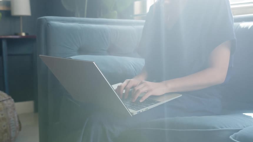 A woman works on a laptop while sitting on a blue sofa indoors