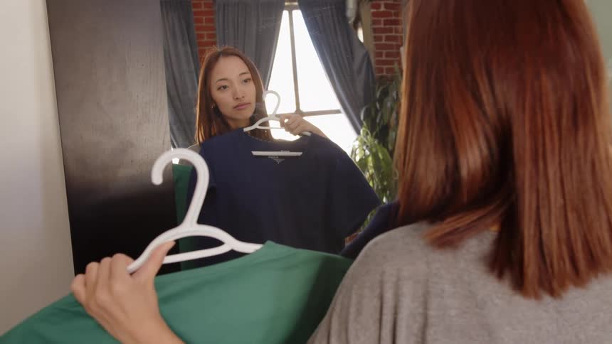 Woman standing in front of a mirror trying on outfits in her bedroom