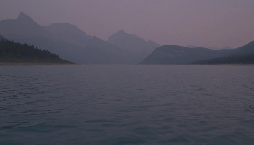 Silhouetted mountains over a lake under an overcast sky at sunset
