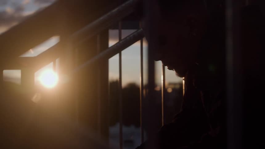 Man in silhouette leans against railing at sunset with blurred horizon in the background