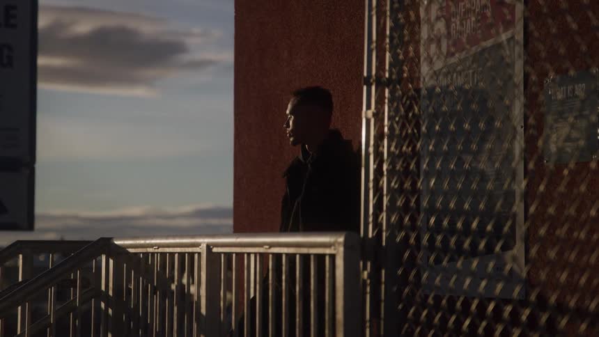 Person on platform with metal railings beside red wall and partly cloudy sky in the background