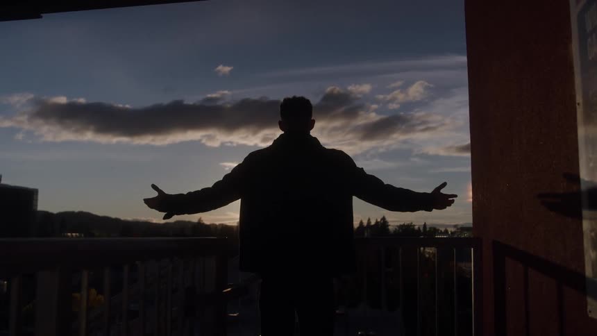 Man standing silhouetted by the rising sun spreads out his arms while facing the sun