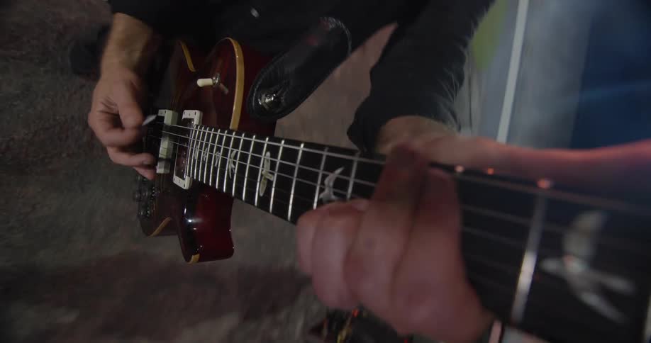 A musicians hands rapidly playing a figured top electric guitar on a dimly lit stage