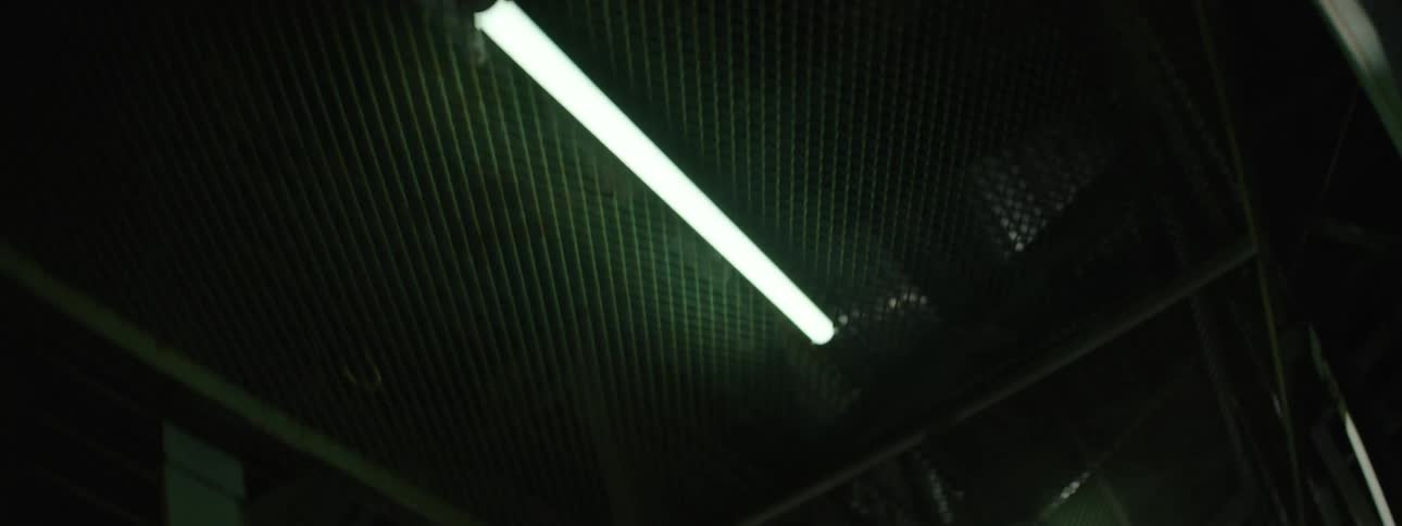 An angled low view reveals the structure and bright fluorescent lights of the dark elevated metal platform and safety mesh at night