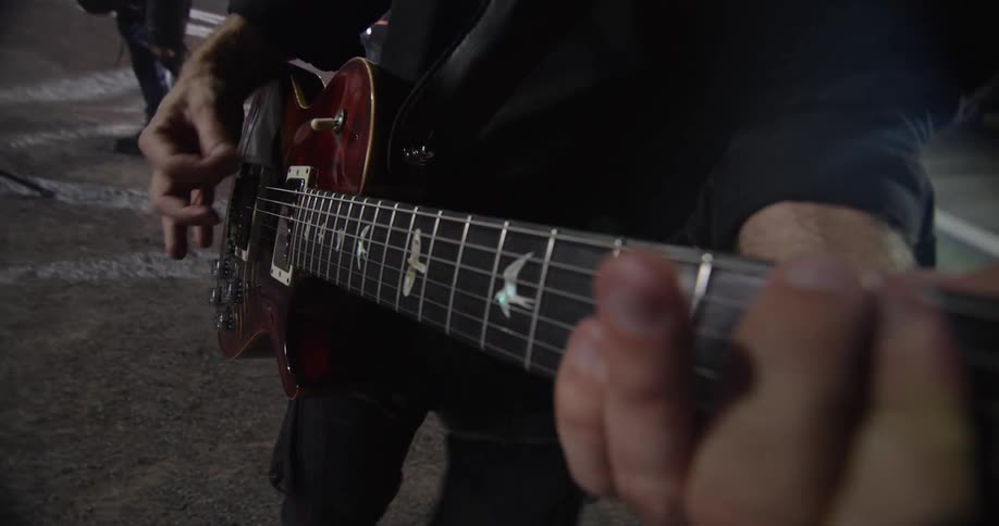 Close up of a male guitarist playing a guitar as part of a band performing at an outdoor night concert