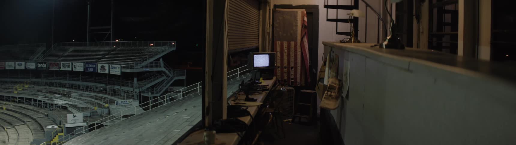 Empty control booth with a lit monitor overlooking the stands at night