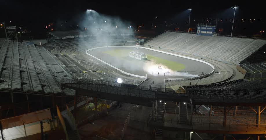 An openroof stadium stands empty at night brightly illuminated by lights