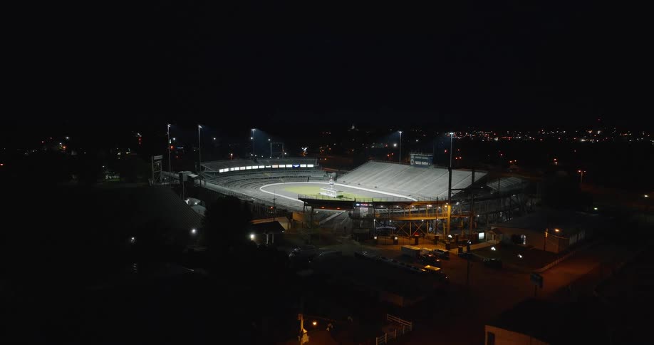 Racetrack illuminated at night with empty stands and city lights in the background