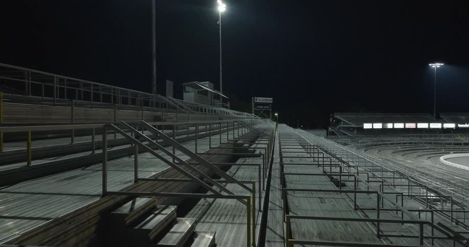 Empty metal bleachers lit by floodlights beside racetrack at night