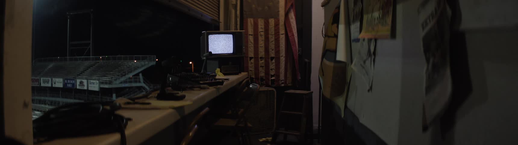 Dark room with a television showing static and a view of lit bleachers in the background