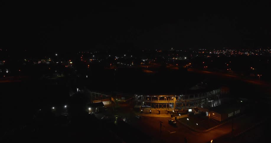 The video is a highangle shot of a small illuminated dirt track stadium at night surrounded by dark residential and urban lights the bright floodlights highlight the empty oval track and the surrounding metal bleachers