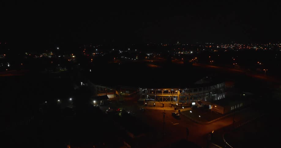 The video is a highangle nighttime aerial shot of a small empty racetrack or speedway the entire stadium area is dimly lit and surrounded by the darkness of the encompassing city