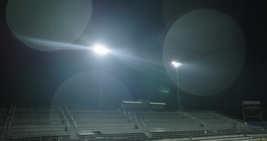 A stadium stands empty at night illuminated by tall floodlights