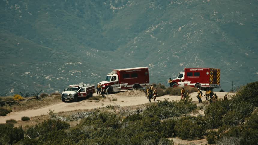 Firefighters work among the scrub on a slope on a hazy day