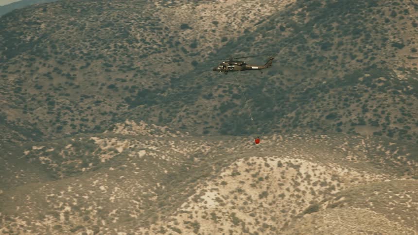 Aerial of a helicopter carrying suspended supplies while flying through the air during daytime