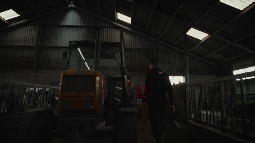 Man walks to the tractor parked in his barn and climbs onboard