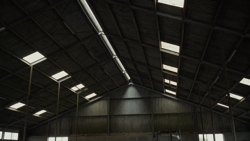 A large corrugated metal barn interior shows a high peaked roof dotted with skylights