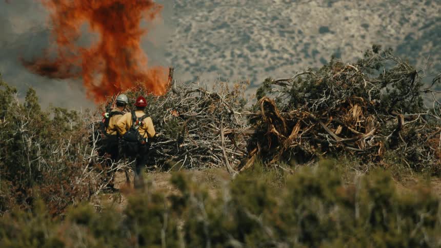 Two firemen overlook damage caused by a brush fire in a dry scrubby landscape