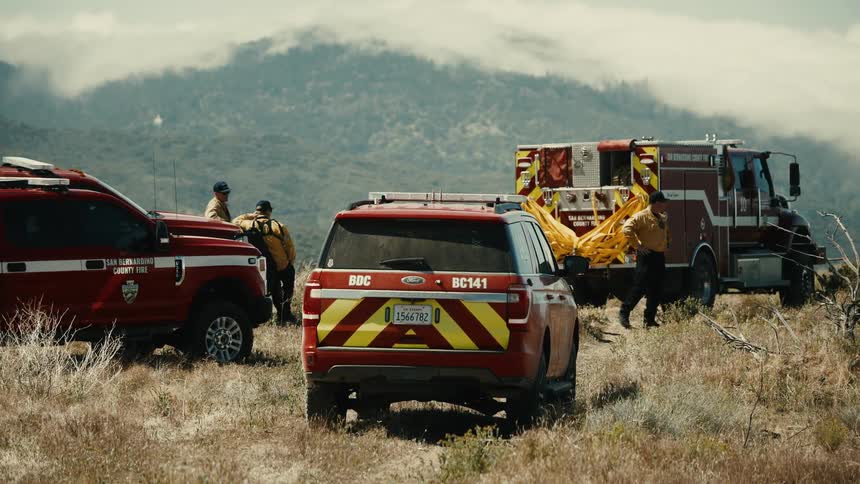 First responders gather on a hillside with emergency vehicles near hazy mountains