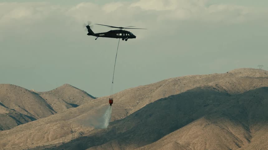 Fire helicopter opens the bucket valve and releases the water over the fire