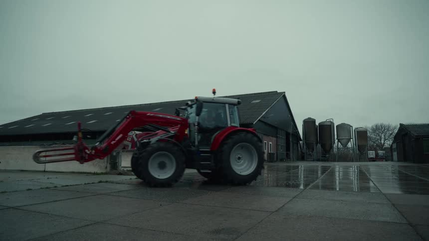 A person drives a tractor from the parking next to a barn