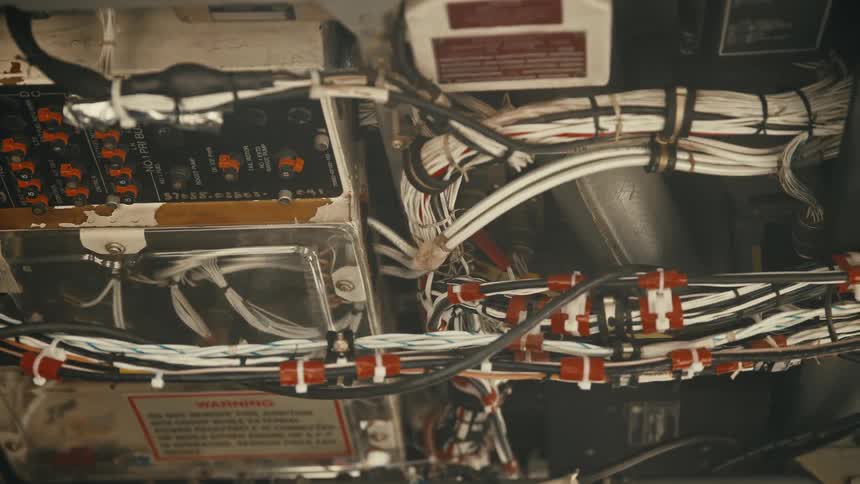 A dense configuration of electrical wiring and cables the bundles of wires are neatly tied together and routed along a metal frame circuit panels and a warning label are visible behind the wires