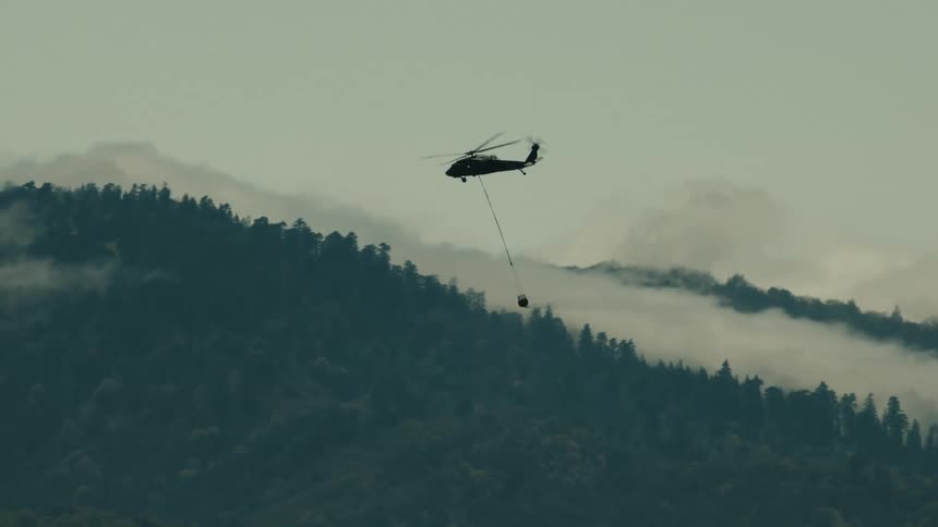 A firefighting helicopter drops water over a forest fire in the mountains