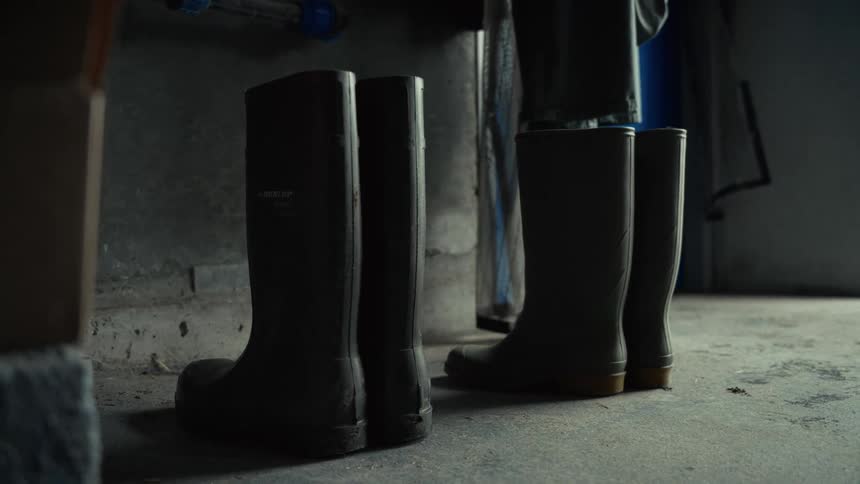 A pair of muddy rubber boots stands beside another pair on a concrete floor beneath a workbench