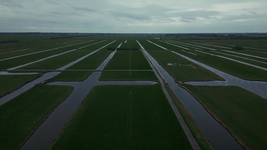 Green fields divided by water channels under a cloudy sky