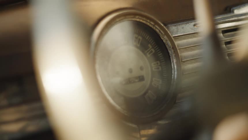 Person steers a classic vehicle with an analog speedometer during the daytime