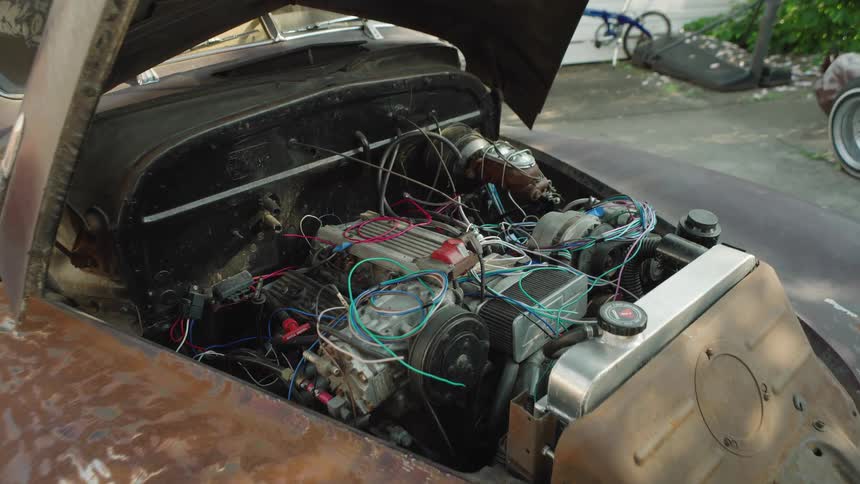 The man points towards the engine in the car