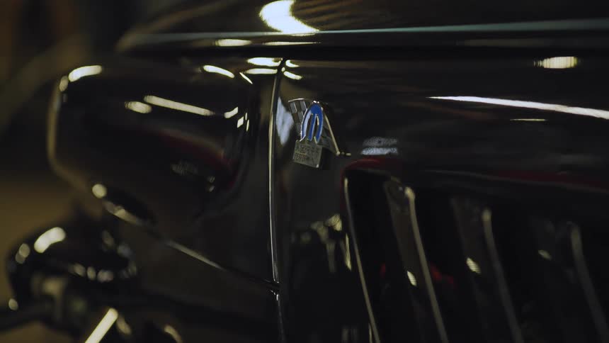 The video is an extreme closeup focusing on the shiny black fender of a classic car the chrome trim and a small emblem on the body are visible reflecting a softly lit interior space