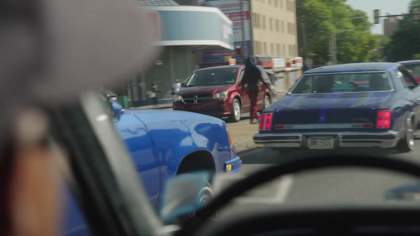 Vintage cars driving down an avenue with a red traffic light ahead