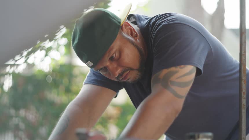 Man in a green cap adjusting a car engine outdoors