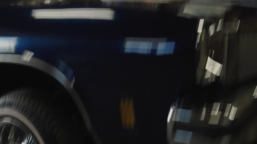 A close low angle view shows the shiny dark blue fender of a lowrider car with chrome wire wheels and whitewall tires parked indoors which is set to bounce and jump using its hydraulic system