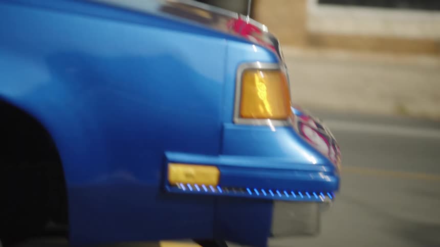Front wheel of blue car in motion with chrome hubcap and whitewall tire
