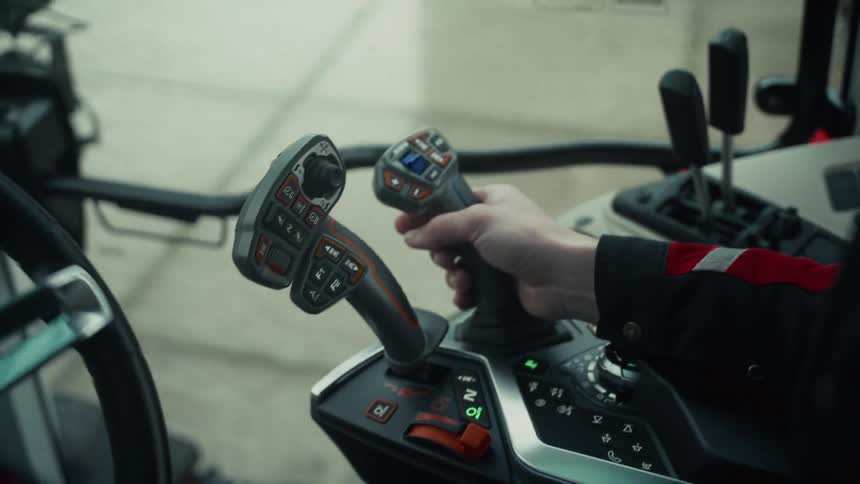 Person operates heavy machinery with hand on multifunction lever in illuminated control panel with buttons and indicators